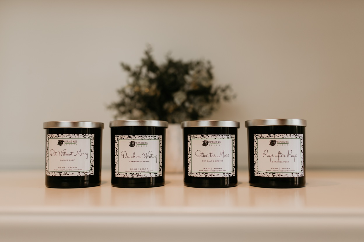 Four candles in black sontainers. Two are lit and lying on their sides. Plant in background.