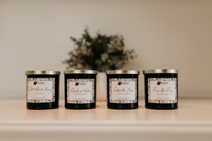 Four candles in black sontainers. Two are lit and lying on their sides. Plant in background.